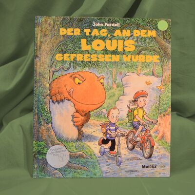 Foto des Buches "Der Tag, an dem Louis gefressen wurde". Das Cover zeigt im Vordergrund zwei Kinder, die durch einen Wald fahren. Das gr&ouml;&szlig;ere M&auml;dchen f&auml;hrt auf einem Fahrrad, der kleinere Junge auf einem Tret-Roller. Im Hintergrund lauert ein zwar freundlich gezeichnetes, aber hungriges Ungeheuer.