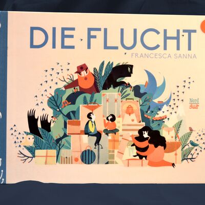 Foto des Buchs "Die Flucht". Das Cover zeigt viele grafische Details aus dem Inhalt; im Mittelpunkt eine Familie vor Bergen von gepackten Koffern und Kartons.