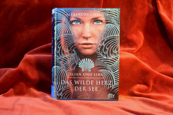 Foto des Buches "Das wilde Herz der See". Das Cover zeigt das Gesicht einer jungen Frau, umgeben von grafischen Wellen. Unter ihrem Kinn ist eine Muschel abgebildet, darunter steht der Buchtitel.