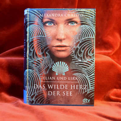 Foto des Buches "Das wilde Herz der See". Das Cover zeigt das Gesicht einer jungen Frau, umgeben von grafischen Wellen. Unter ihrem Kinn ist eine Muschel abgebildet, darunter steht der Buchtitel.