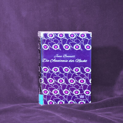 Foto des Buches "Die Anatomie der Nacht". Das Cover zeigt ein grafisches Muster in den Farben lila, wei&szlig; und rosa.