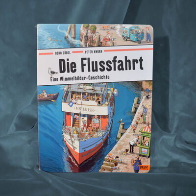 Foto des Pappbilderbuches "Die Flussfahrt". Das Cover zeigt ein wimmelig gezeichnetes Bild mit einem ablegenden Ausflugsschiff.