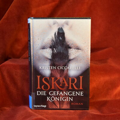 Foto des Buches "Die gefangene K&ouml;nigin". Der Hintergrund des Covers zeigt die untere H&auml;lfte eines Frauengesichts, das sich eine lange Feder senkrecht &uuml;ber die Lippen h&auml;lt.