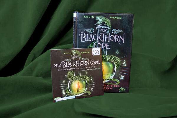 Foto des Buchs und H&ouml;rbuchs "Der Blackthorn-Code - das Verm&auml;chtnis des Alchemisten". Das Cover zeigt ein bauchiges Glasgef&auml;&szlig;, um das sich eine Schlange windet. Im Inneren des Glases ist ein helles Licht zu erkennen, davor die Silhouette eines Jungen.