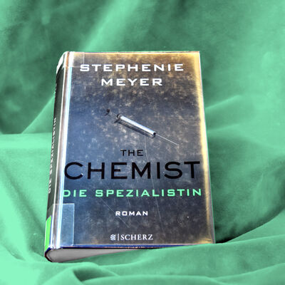 Buchfoto; das silbrige Metallic-Cover zeigt eine Spritze und darunter den Buchtitel "The Chemist - Die Spezialistin".