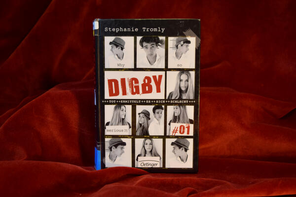 Foto des Buches "Digby". Das Cover zeigt mehrere Schwarz-Wei&szlig;-Fotos von einem Jungen mit Hut und einem langhaarigen M&auml;dchen. Der Titel "Digby #1" ist mittig in Rot eingef&uuml;gt, sowie die Zeile "Tot ermittelt es sich schlecht".