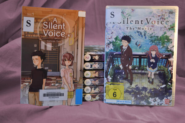 Foto der siebenb&auml;ndigen Mangareihe "A silent voice" und der gleichnamigen DVD. Auf dem Cover des ersten Bandes und dem Cover der DVD sind jeweils die beiden Hauptfiguren Shoya und Shoko zu sehen - beim Manga als Kinder in der Grundschule, beim Film als Jugendliche auf einer Br&uuml;cke.