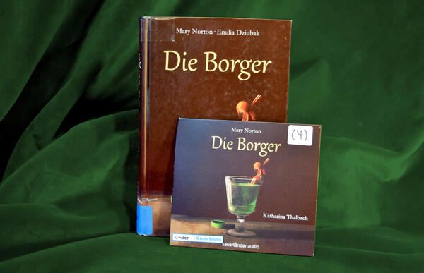 Foto des Buches "Die Borger" und des gleichnamigen H&ouml;rbuchs. Das gezeichnete Cover zeigt ein edles Trinkglas mit Fu&szlig; und gef&uuml;llt mit einem gr&uuml;nen Getr&auml;nk. Oben auf dem Rand des Glases sitzt ein winziges M&auml;dchen und l&auml;sst die F&uuml;&szlig;e ins Getr&auml;nk baumeln. Die Haare des M&auml;dchens werden von einer W&auml;scheklammer zusammengehalten.
