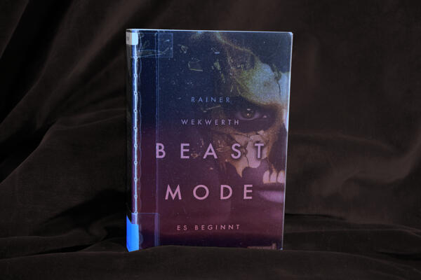 Foto des Buches "Beast Mode - Es beginnt". Das Cover zeigt ein dunkles Gesicht mit einer zersplitternden goldenen Maske.