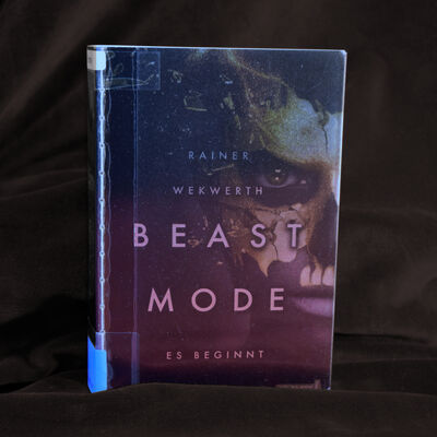 Foto des Buches "Beast Mode - Es beginnt". Das Cover zeigt ein dunkles Gesicht mit einer zersplitternden goldenen Maske.