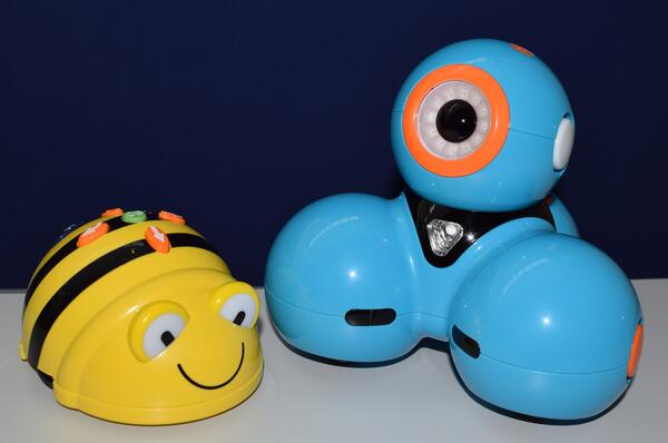 Foto der bibliothekseigenen Roboter "Bee-Bot" (in Form einer gro&szlig;en Biene) und "Dash" (sieht aus wie mehrere in Dreiecksform miteinander verbundene hellblaue Kugeln).