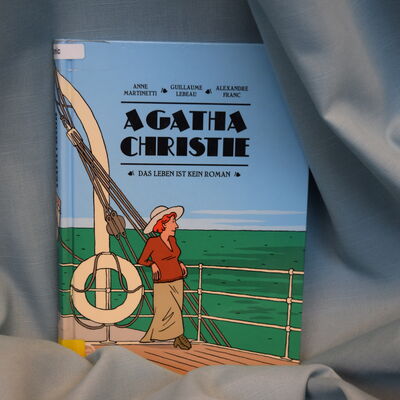Foto des biografischen Comics "Agatha Christie - das Leben ist kein Roman". Das Cover zeigt eine Comiczeichnung, auf der Agatha Christie neben einem Rettungsring an Deck eines Schiffes steht und aufs Meer schaut.