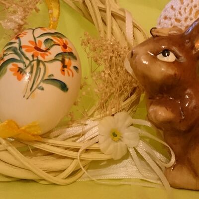 Foto mehrerer Ostereier, eines hellen Osterkranzes und eines braunen Porzellan-Osterhasen.