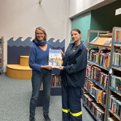 Das Foto zeigt Lucy Thomsen und Susanne Luther-Feddersen bei der &Uuml;bergabe der THW-Buchspende in der Kinder-Abteilung der Bibliothek.
